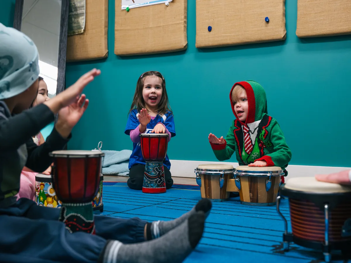 Kids seated on the floor with djembes and bongos, smiling and playing during a group class at Resonate