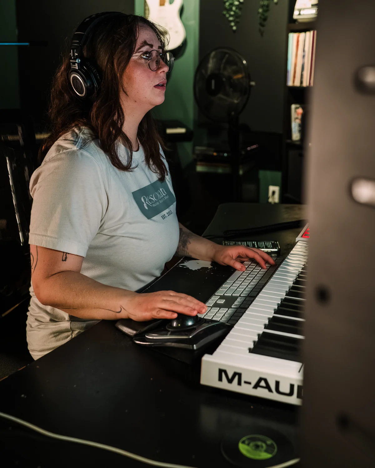 Producer at the Resonate desk wearing headphones, hands on the MIDI keyboard during a production session in Edmonton